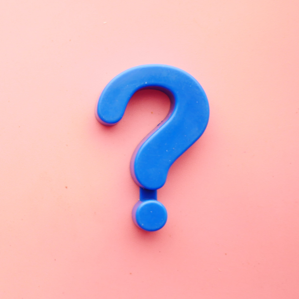 giant blue plastic question mark on a faded salmon pink background