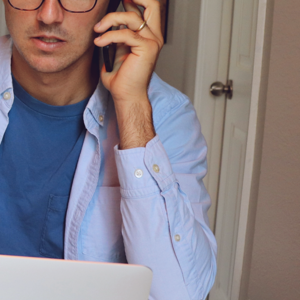middle aged man in a blue shirt looking at his laptop while on the phone