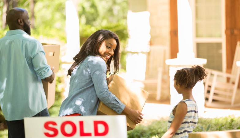 Action shot of family moving boxes near "sold" sign